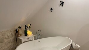 Un baño moderno con una bañera independiente, un tocador blanco con espejo, una botella de vino y una vela.