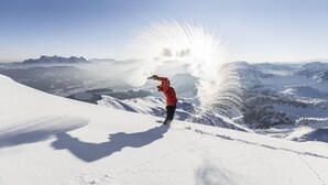 En person i en röd jacka på ett snötäckt berg med en klar himmel.