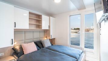 Un dormitorio moderno con cama, mesitas de noche, armario empotrado y vistas al mar a través de un ventanal.