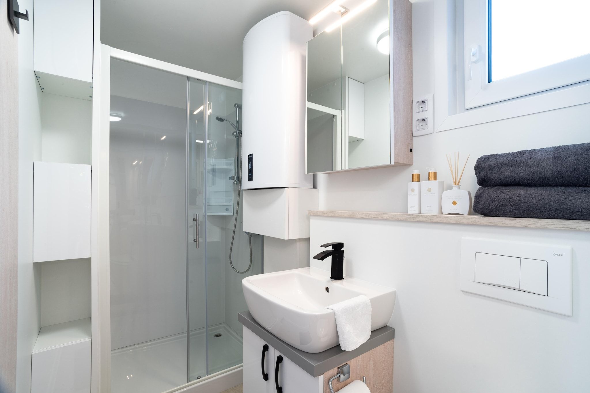 A modern bathroom with a glass-enclosed shower, a white sink with a black faucet, and a mirror above the sink.
