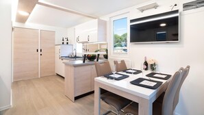 Une cuisine moderne avec un coin repas, des meubles en bois, un four encastré et un téléviseur fixé au mur.
