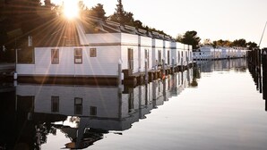 Une rangée de maisons mobiles blanches, dotées de fenêtres, reliées à une jetée par un canal.