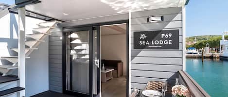 A modern Sea Lodge with a glass door entrance, a dining area with a table set for two, and a view of the marina.