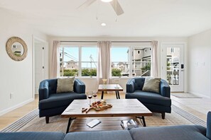A modern living room with two sofas, a coffee table, and a view of neighboring houses through large windows. - Waterfront - Sauna -Steps To Beach! (Saco)