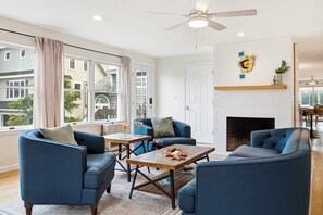 A modern living room with a fireplace, blue furniture, and a view of neighboring buildings. - Waterfront - Sauna -Steps To Beach! (Saco)