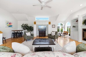 A spacious living room with a high ceiling, a ceiling fan, a dining area with a table and chairs, and a kitchen with a large window. - Waterfront - Sauna -Steps To Beach! (Saco)