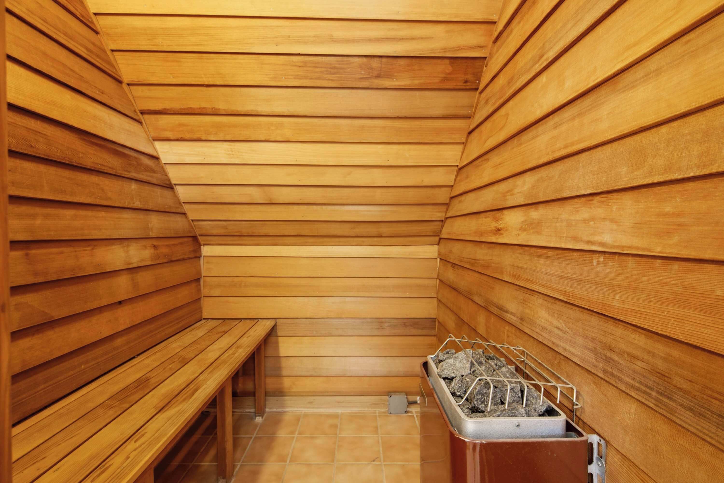 Una sauna amb parets i bancs de fusta, un sòl de rajola i un recipient metàl·lic amb pedres.