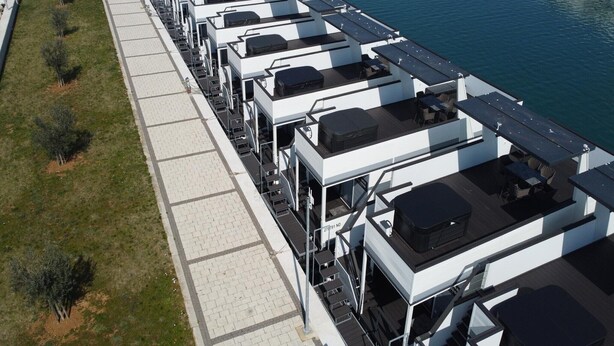 Una fila de habitaciones de hotel modernas y compactas con balcones con vistas a un cuerpo de agua.