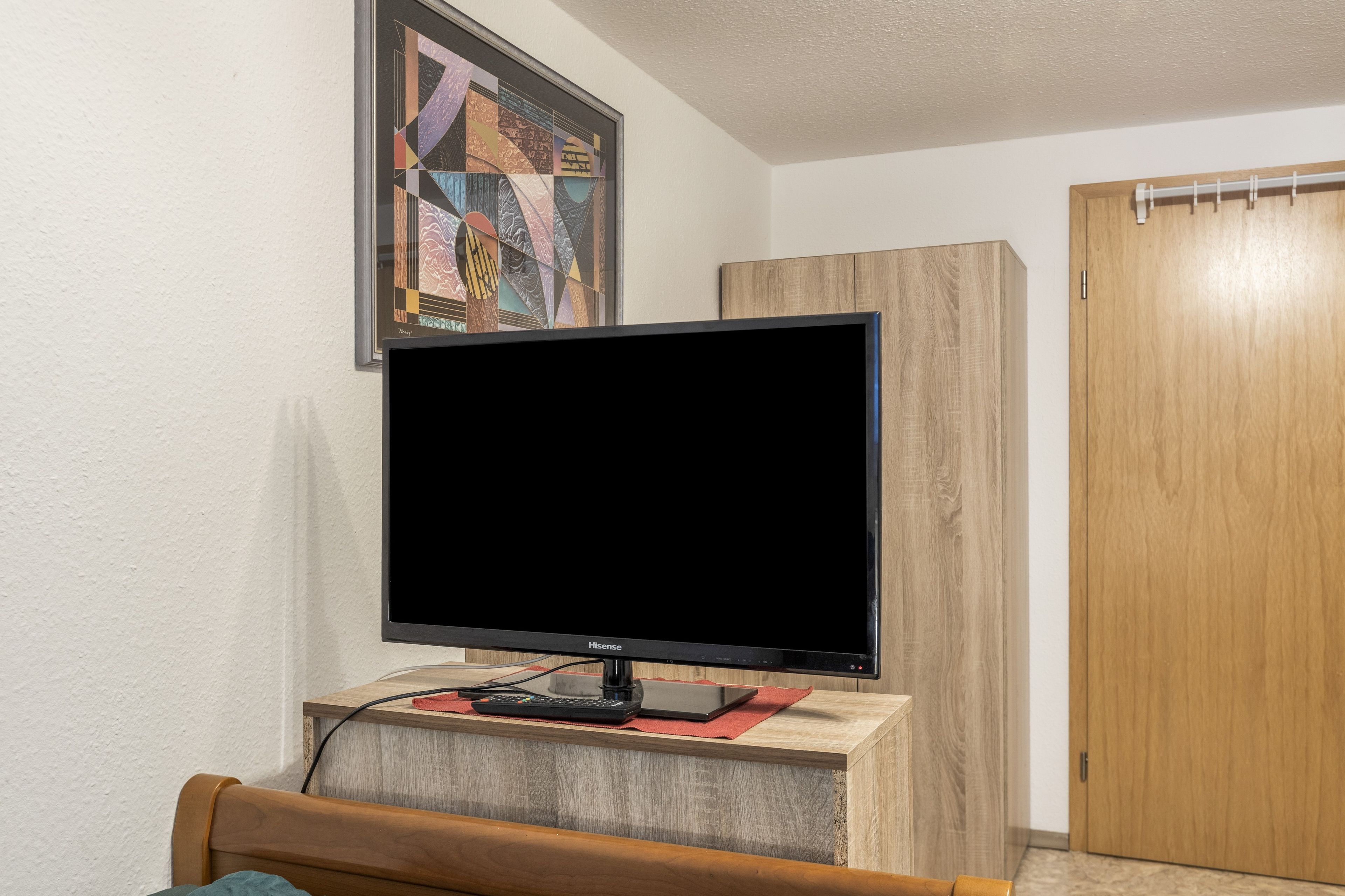 A room with a flat-screen TV on a wooden stand, a wooden door, and a wall-mounted artwork.