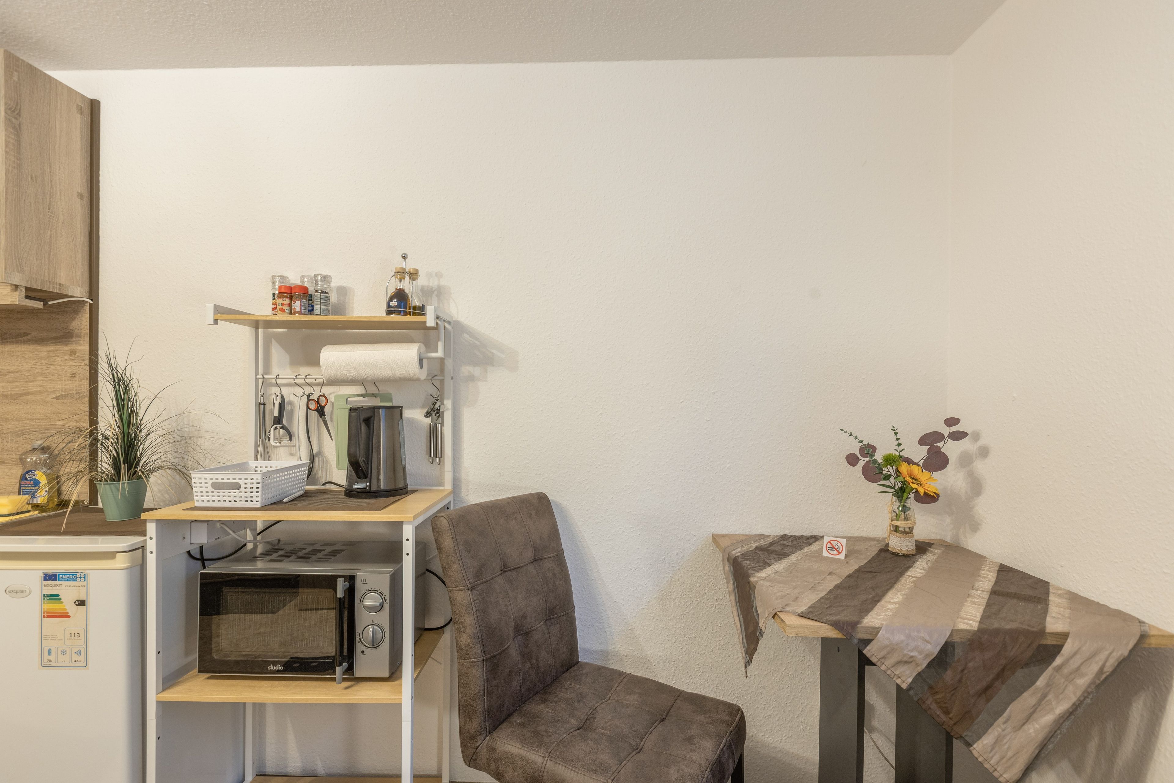 Uma cozinha compacta equipada com micro-ondas, cafeteira e prateleiras para armazenamento.