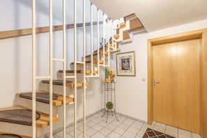 Eine Treppe mit Holzboden und weißen Geländern, eine Tür sowie ein kleiner Tisch mit einer Pflanze.
