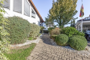 A paved pathway leading to a white building with shutters, surrounded by well-maintained hedges and a flagpole with a flag. - '1 Room - Apartment Basement Floor' with Wi-Fi (Hüfingen)