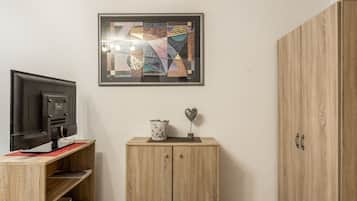 Ein Zimmer mit einem Fernseher auf einem Schrank, einem Schrank mit einer Blumenvase und einem gerahmten abstrakten Kunstwerk an der Wand.