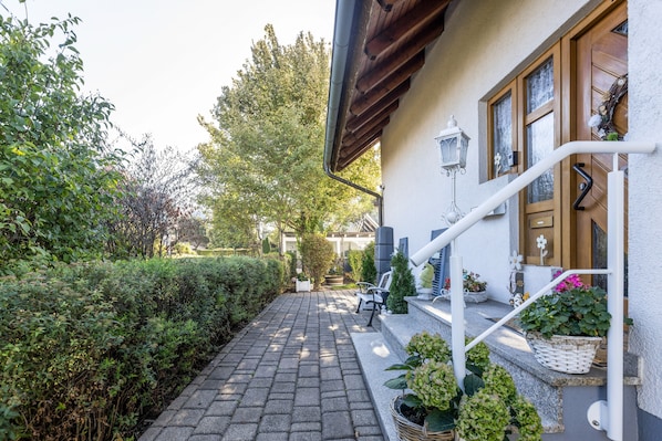 A paved pathway leading to a building with a wooden door and windows, surrounded by greenery and a small bench. - '1 Room - Apartment Basement Floor' with Wi-Fi (Hüfingen)