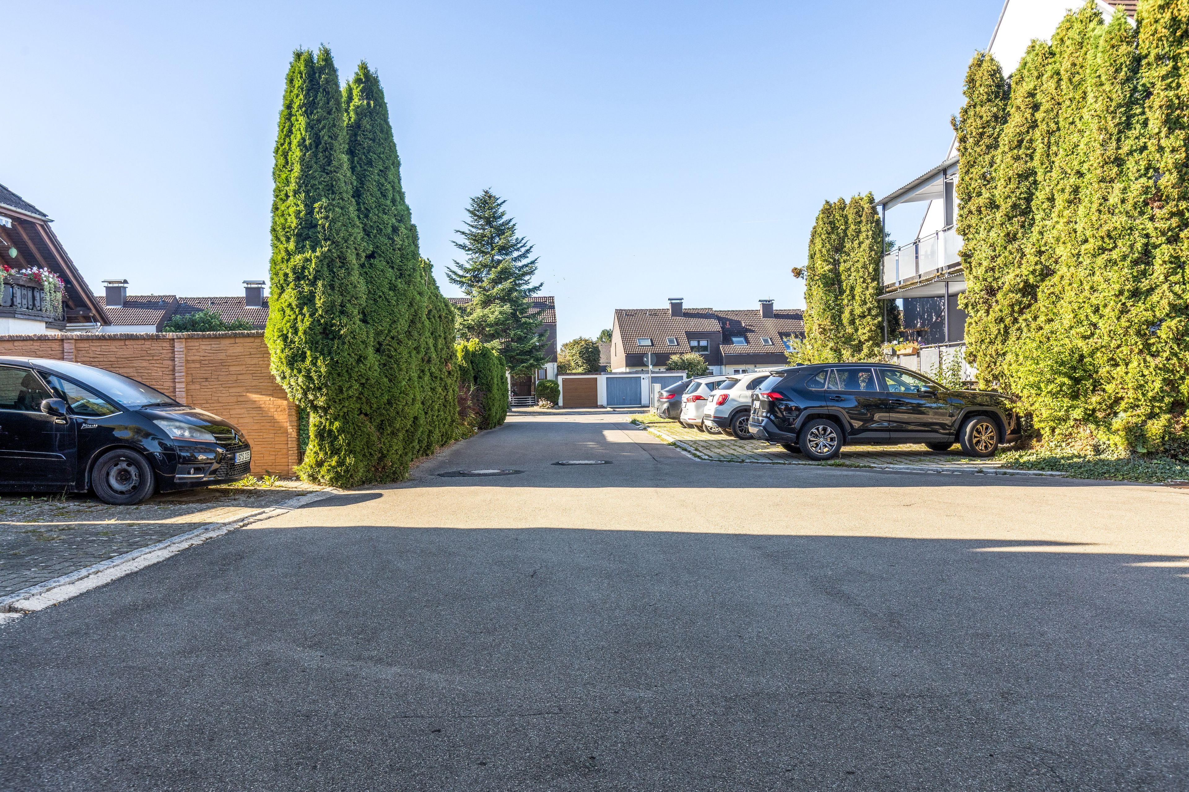 A parking lot with cars and tall trees, a building with a sloped roof, and a clear sky.