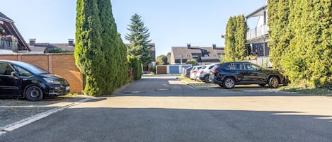 A parking lot with cars and tall trees, a building with a sloped roof, and a clear sky.