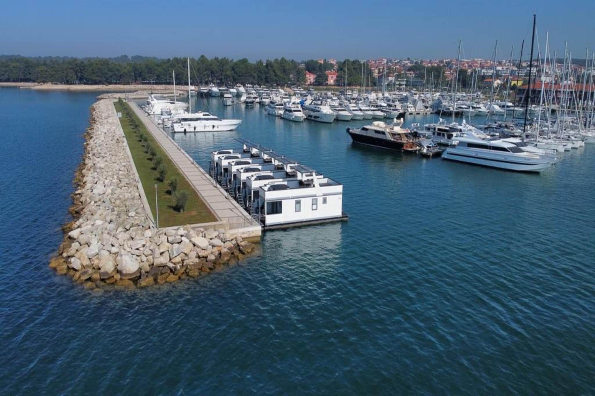 Un puerto deportivo con barcos amarrados, un edificio junto al muelle y un rompeolas rocoso.