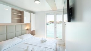 Una camera d'albergo con un letto, una TV fissata al muro, una finestra vista mare e uno scaffale a incasso.