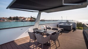 Una terrazza esterna con tavolo e sedie, una vasca idromassaggio e vista sull'acqua e sugli edifici.
