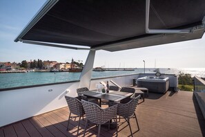 Eine Außenterrasse mit Tisch und Stühlen, einem Whirlpool und Blick auf Wasser und Gebäude.