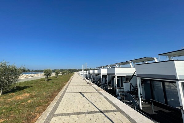 A row of modern hotel rooms with large windows, a paved walkway, and a view of the sea. - Dream houseboat with sea view and hot tub (Novigrad)