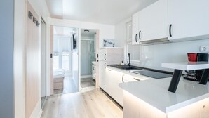 Eine moderne Küche mit weißen Schränken, einer schwarzen Arbeitsplatte und Blick ins Freie durch eine Tür.