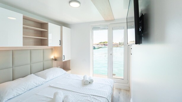A hotel room with a bed, a TV mounted on the wall, a window with a view of the sea, and a built-in shelf. - Dream houseboat with sea view and hot tub (Novigrad)