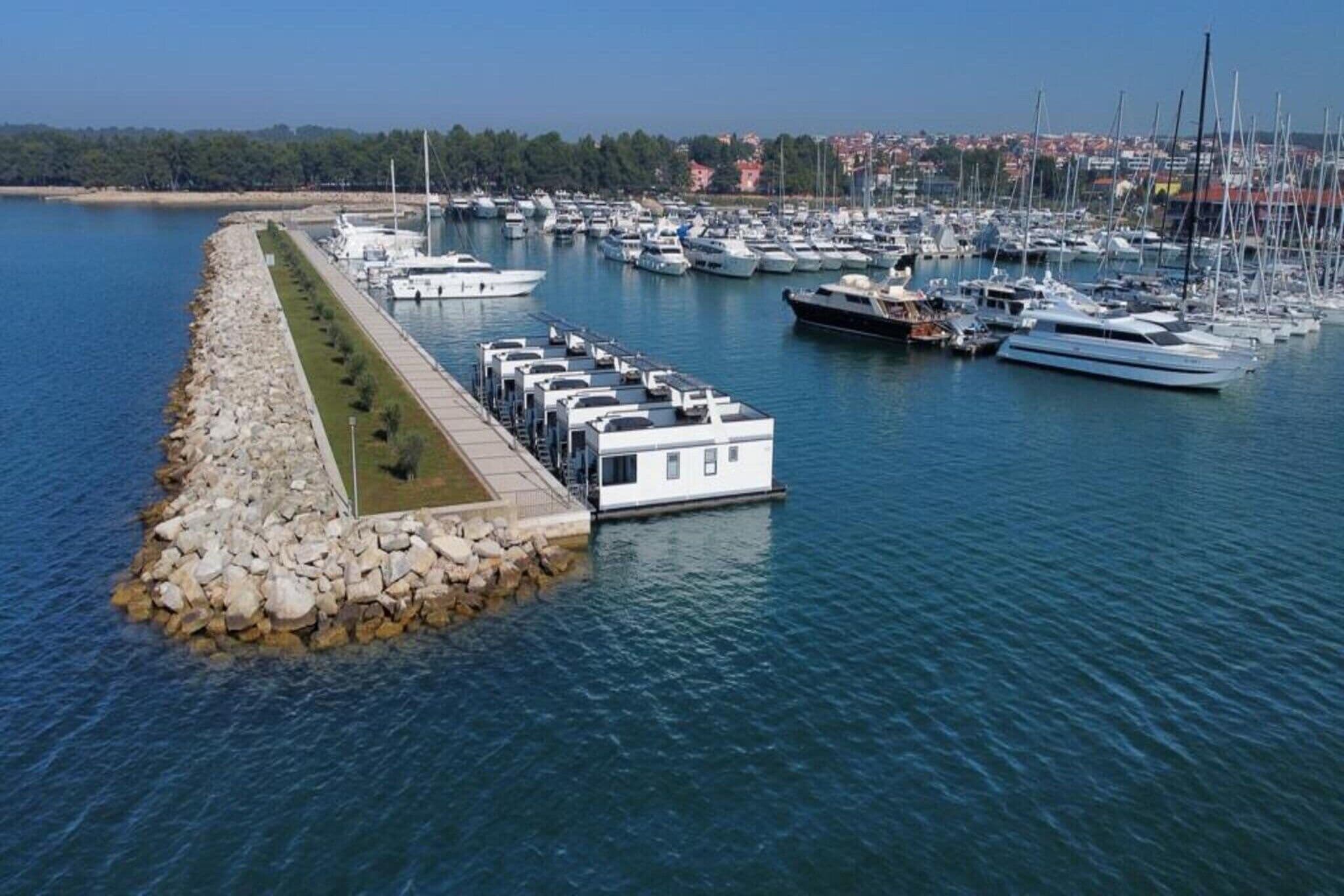 Puerto deportivo con barcos amarrados, un rompeolas de piedra y una hilera de edificios a lo largo de la orilla.