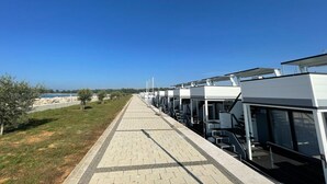 A row of modern hotel rooms with large windows, a paved walkway, and a view of the sea. - Dream houseboat with sea view and hot tub (Novigrad)