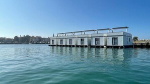 Uma fileira de casas flutuantes, com vista clara para a água e uma linha de costa distante.