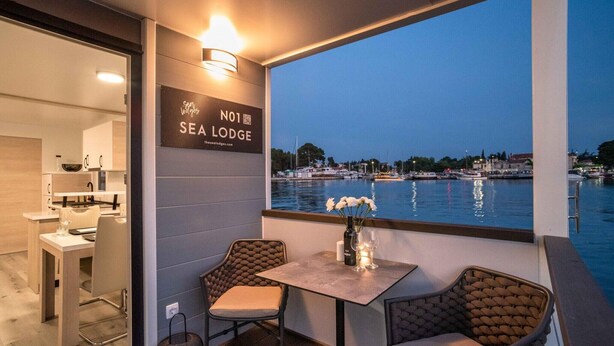 Uma área de refeições com vista para o mar, um letreiro com a inscrição 'Sea Lodge' e uma mesa com cadeiras.