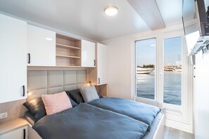 Ein modernes Schlafzimmer mit Bett, Nachttischen, einem Einbauschrank und Meerblick durch eine Glastür.