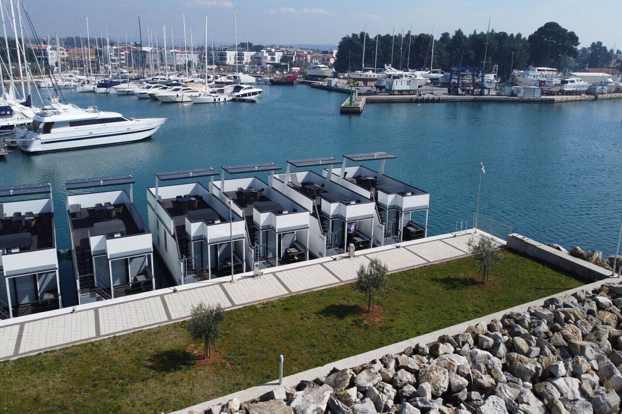 Un puerto deportivo con varias embarcaciones amarradas, un edificio moderno con terraza y una vista despejada del agua.