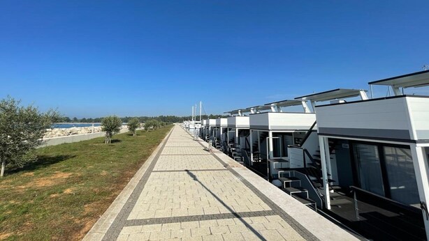 Eine Reihe moderner Hotelzimmer mit großen Fenstern, einem gepflasterten Weg und Blick auf das Meer.