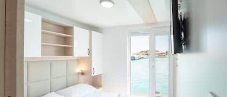 A hotel room with a bed, a TV, and a view of the sea.