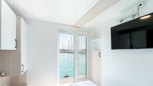 Ein modernes Hotelzimmer mit einem Bett, einem Fernseher und Blick auf einen Jachthafen.