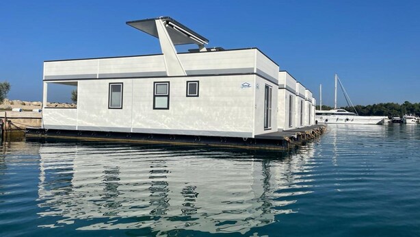 Una casa flotante moderna con techo plano, ventanas grandes y una pequeña terraza.