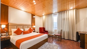 Een hotelkamer met een groot bed, een bureau, een stoel en uitzicht op het omliggende landschap.