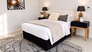 A bedroom with a large bed, two bedside tables, a decorative wall piece, and a patterned rug.