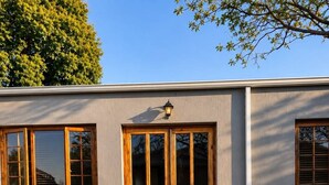 A patio with a stone pathway leading to a double wooden door, outdoor furniture, and a small tree.