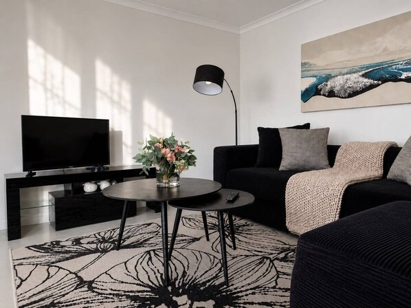 A modern living room with a flat-screen TV, a round coffee table, a sofa, and a painting on the wall.