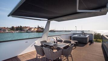 Une terrasse avec une table et des chaises, un jacuzzi et une vue sur l’eau et les bâtiments.