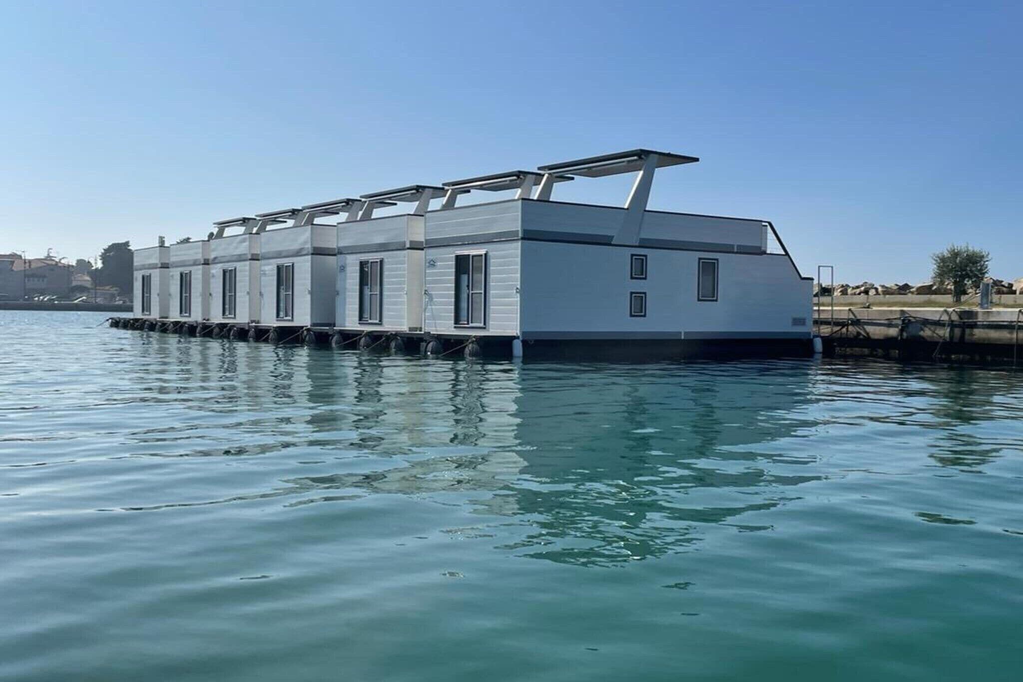 Una casa flotante anclada en un muelle, con techo plano y varias ventanas.