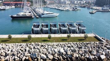 Un puerto deportivo con varias embarcaciones amarradas, un rompeolas rocoso y una hilera de edificios modernos de techos planos.