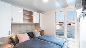 A modern bedroom with a bed, bedside tables, a built-in wardrobe, and a view of the sea through a glass door.