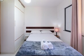 Ein Hotelzimmer mit Bett, Nachttisch mit Lampe, Fenster mit Vorhängen und Handtuch auf dem Bett.
