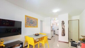 A modern living room with a flat-screen TV, a dining table with yellow chairs, and a colorful abstract painting on the wall. - Apt in a Seaside Condominium With a Pool - Gsh2101 (Camaçari)