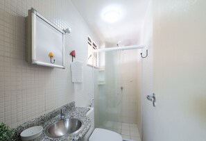 Ein Badezimmer mit Marmorwaschtisch, Toilette in Weiß, einer Duschkabine und einem Spiegel über dem Waschbecken.