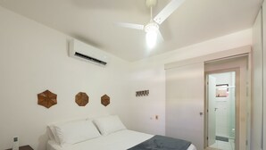 A bedroom with a bed, a bedside table, a ceiling fan, and a door leading to a bathroom. - Apt in a Seaside Condominium With a Pool - Gsh2101 (Camaçari)