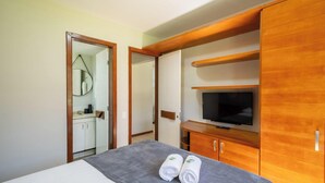 A hotel room with a bed, a TV, a mirror, and a bathroom visible through an open door. - Apt in Condo With Pool Near the Beach Gsh0101 (Camaçari)